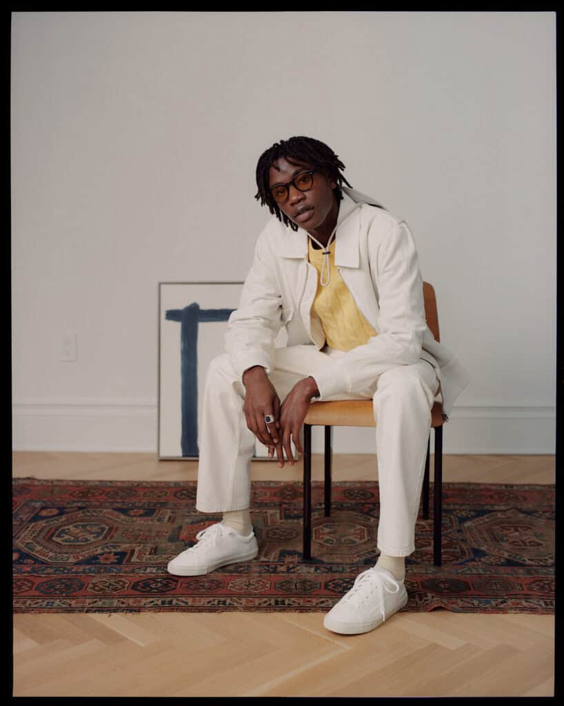 Stylish man in ZARA outfit sitting on a chair in NYC apartment.