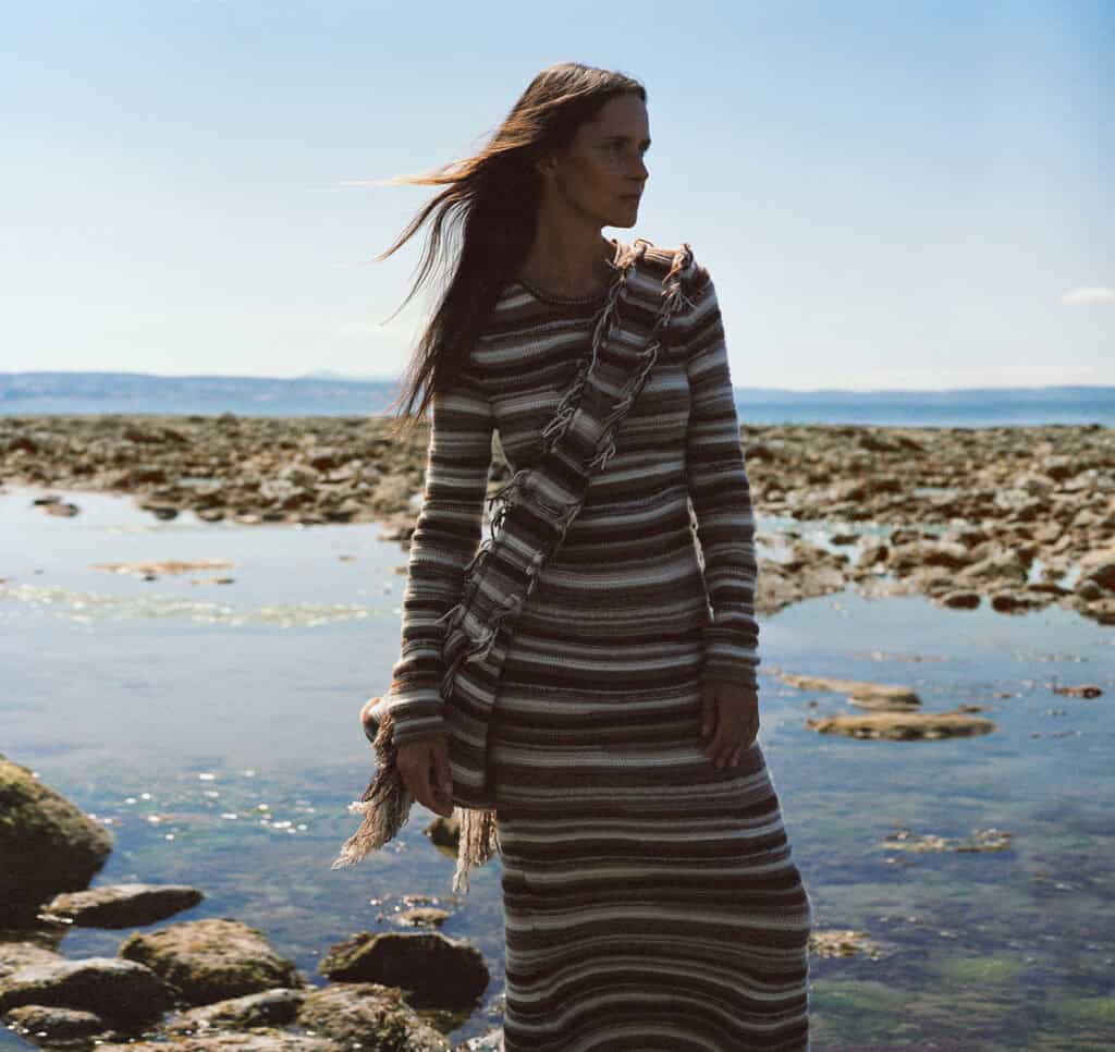 Woman standing by the water in a striped dress and scarf.