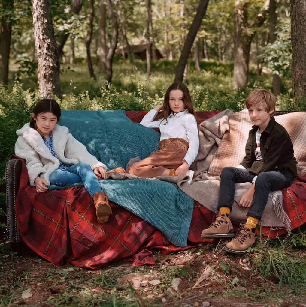 Children sitting on a sofa outdoors in a forest setting for Mango Kids 2019 campaign.