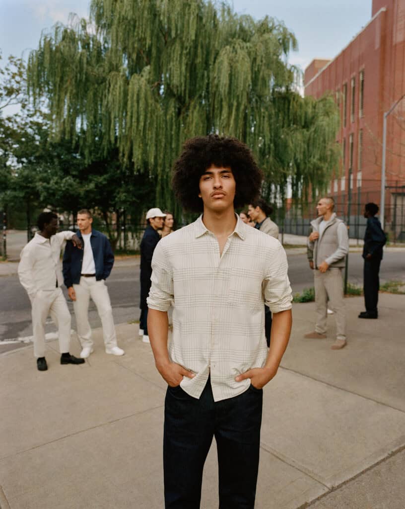 Young man with curly hair posing outdoors in Brooklyn, NY, during daytime.