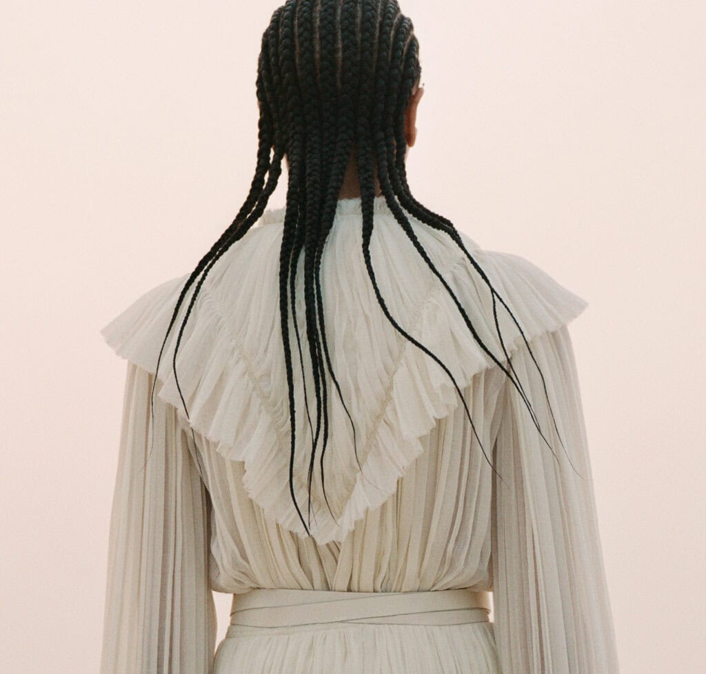Woman with braided hair in elegant cream pleated dress, back view.