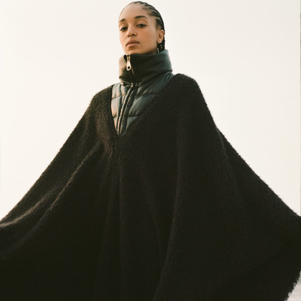Fashion model in black cape with high collar, showcasing modern femininity.