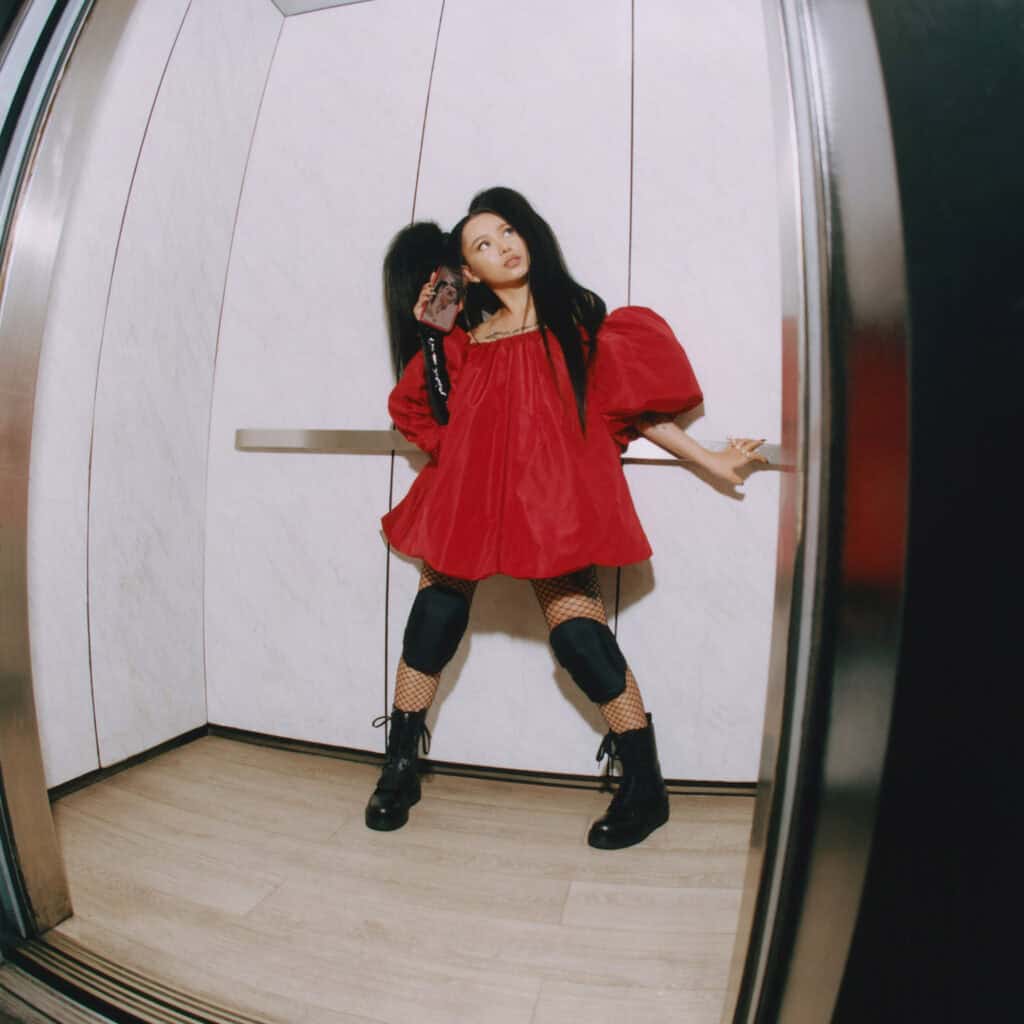 Bella Poach in bold red outfit with fishnet stockings in elevator, fashion editorial.