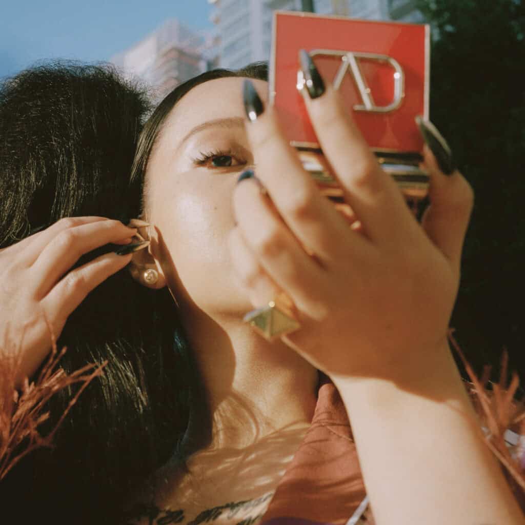 Woman applying makeup outdoors, fashion shoot for Perfect Magazine.