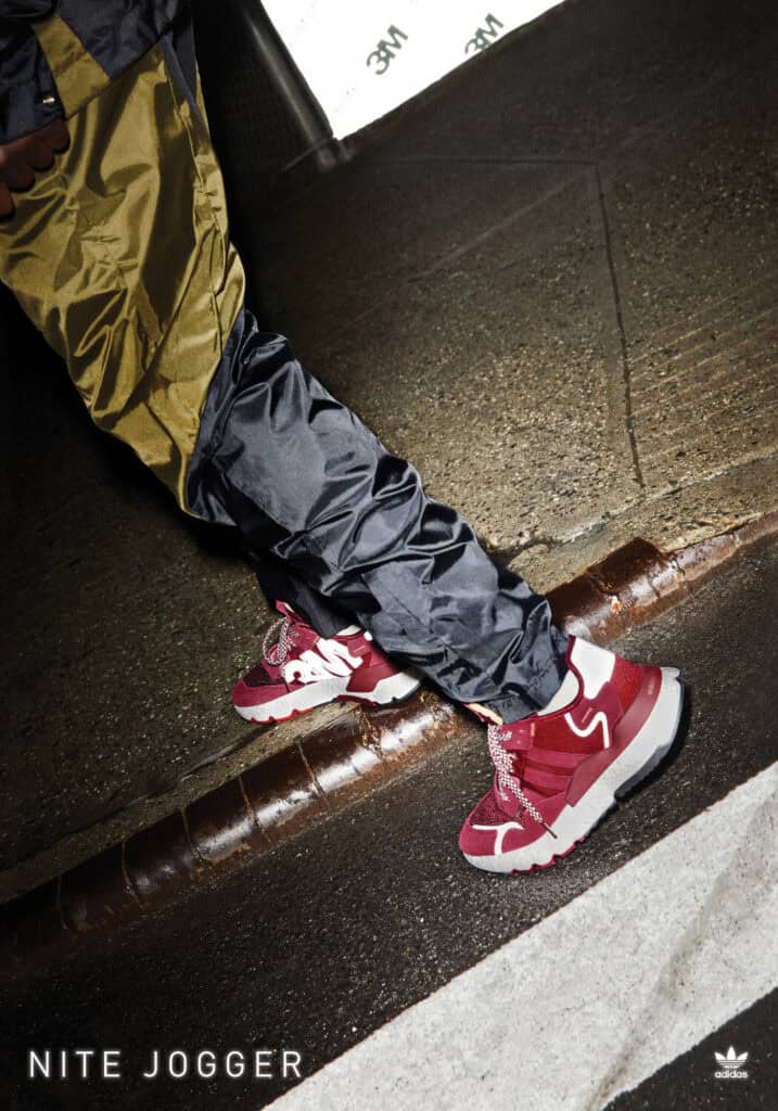 Adidas Nite Jogger sneakers in red and white, worn by a person standing on a city street at night.