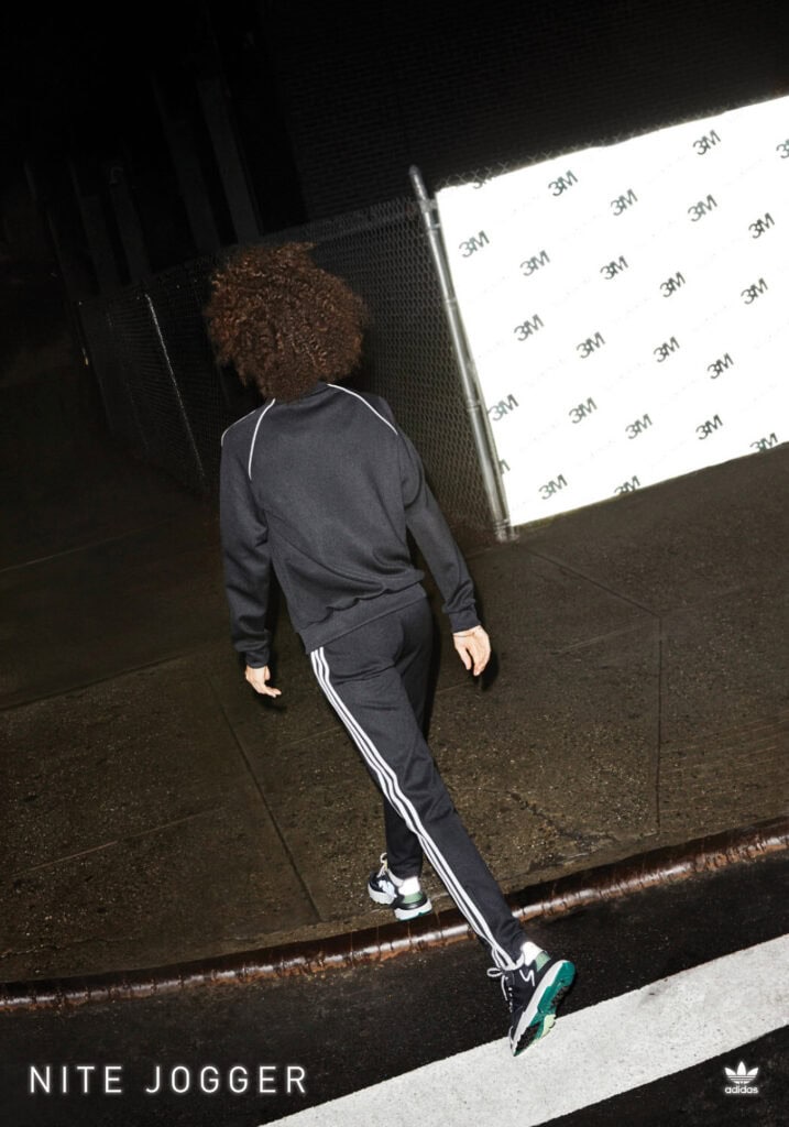Woman walking in Adidas Nite Jogger sneakers at night, urban setting.