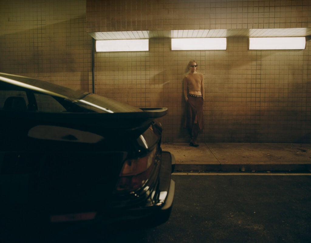 Urban scene featuring a woman in KHAITE Freja 2022 standing against a brick wall at night.