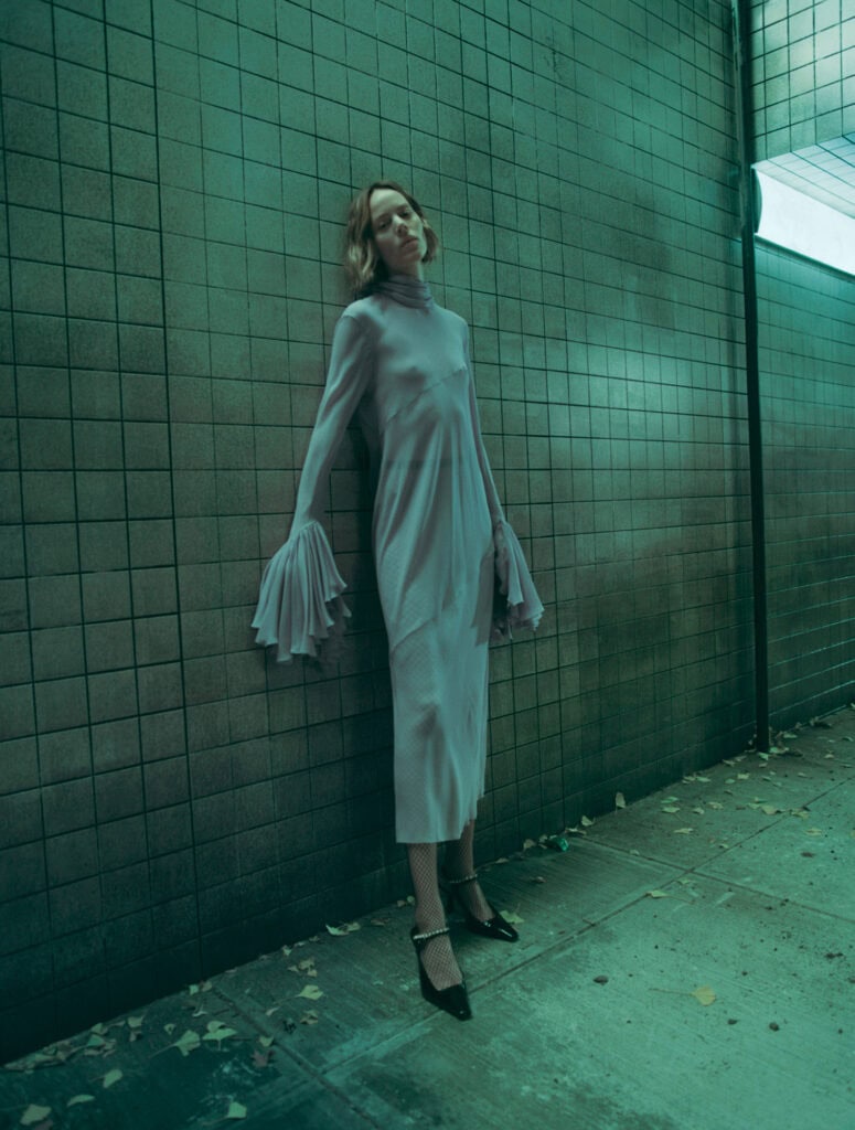 Woman in KHAITE Freja 2022 dress standing against tiled wall.