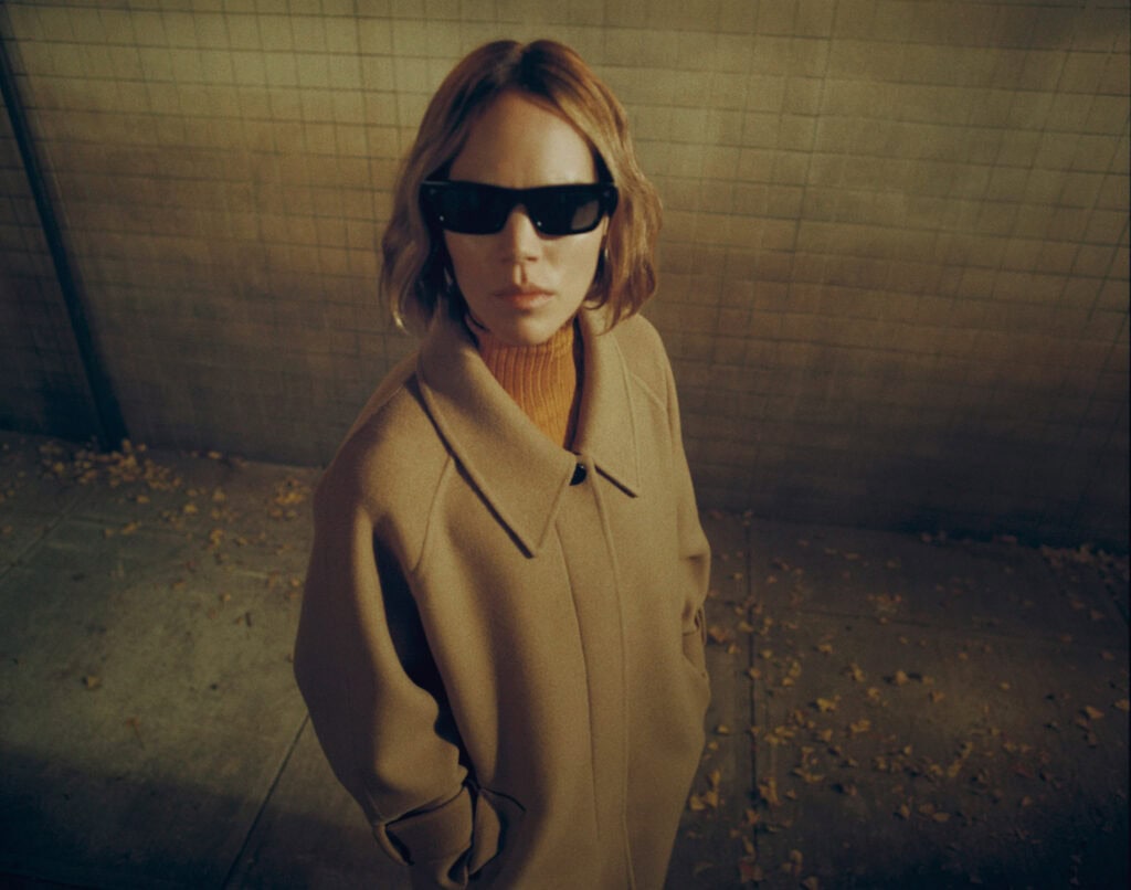 Stylish woman in oversized coat and sunglasses in urban setting.