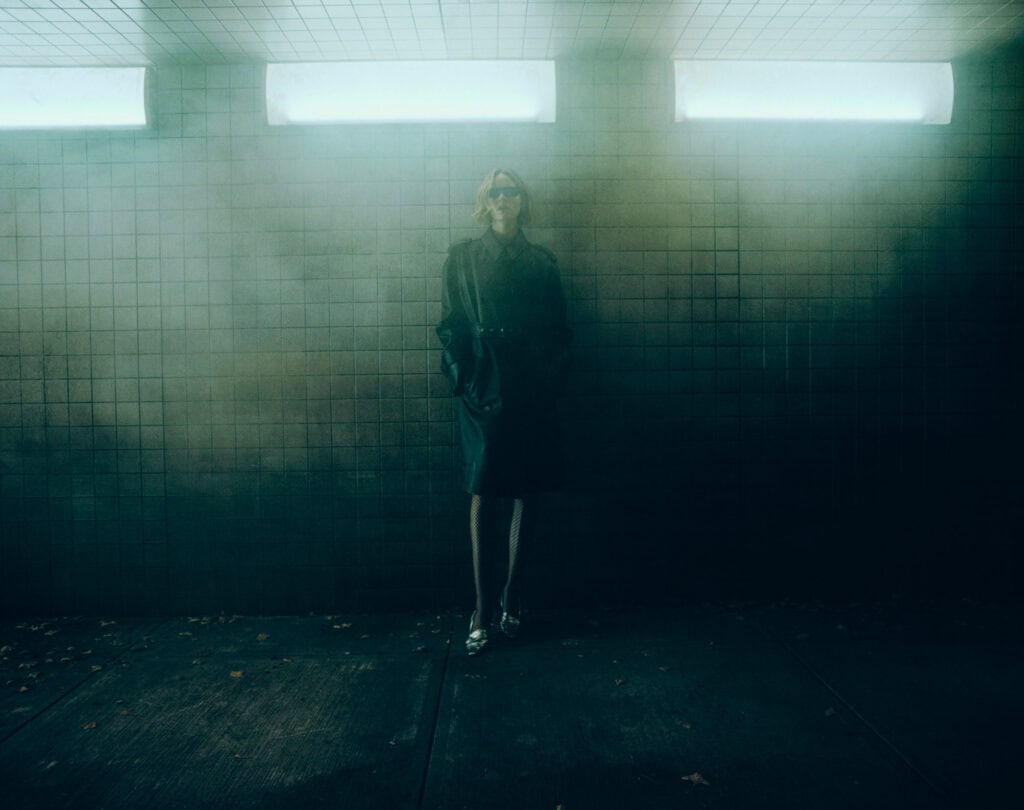 Fashion model in KHAITE Freja 2022 collection standing in a dimly lit, foggy urban setting.