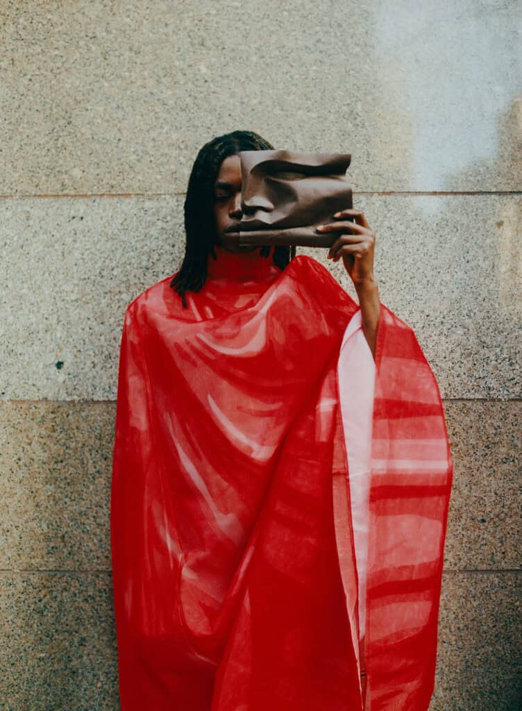 Fashion model wearing a red designer cape and holding a clutch.