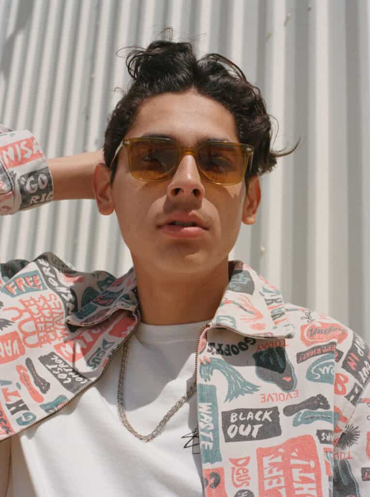 Stylish young man wearing sunglasses and patterned shirt in desert setting.