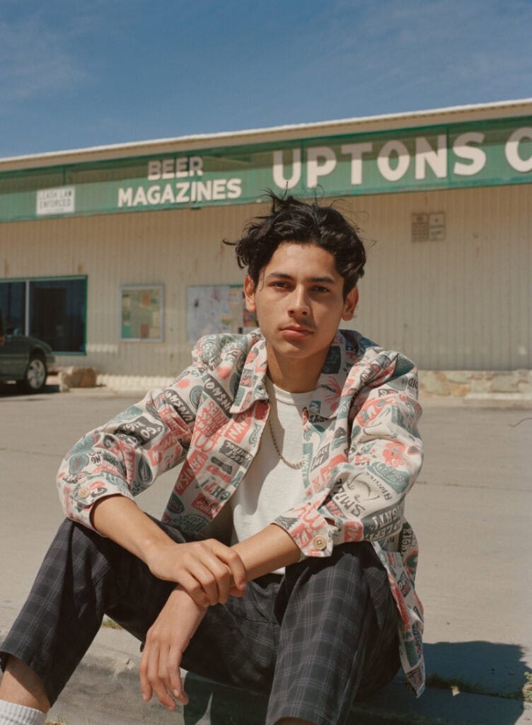 Young man sitting outside a store in desert environment.