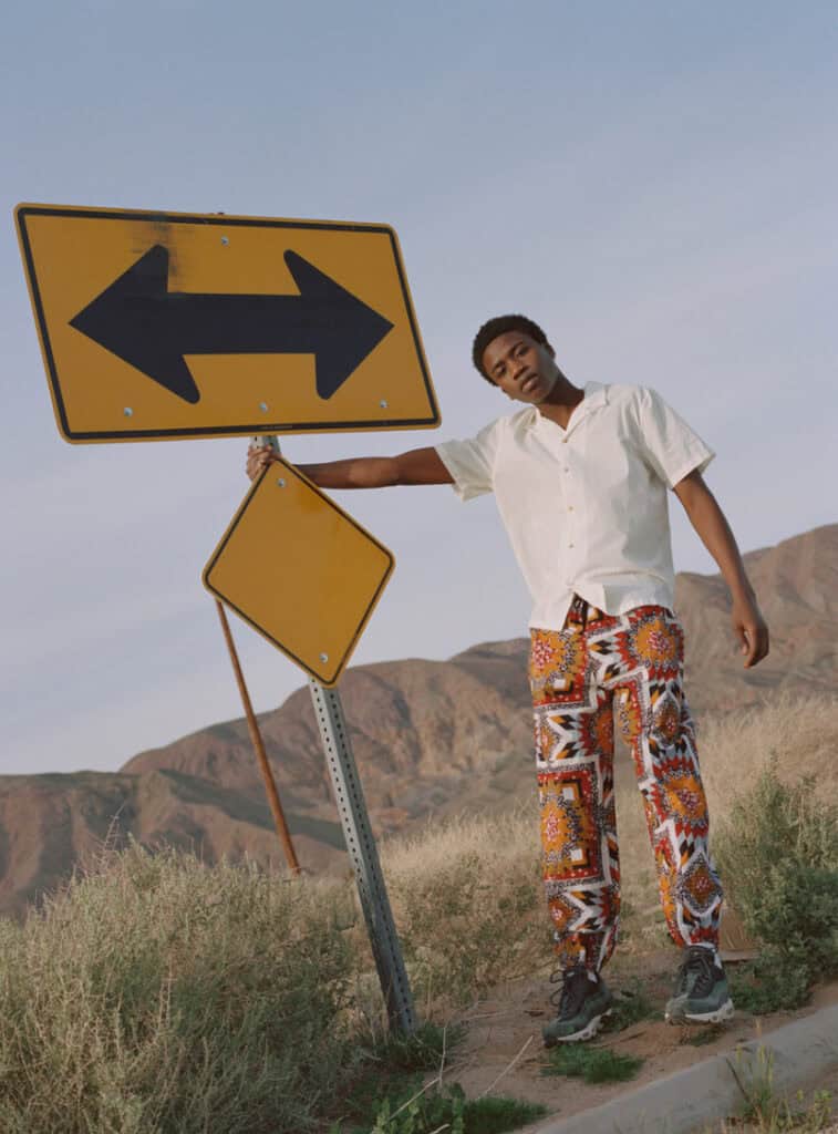 Woman standing next to a directional road sign in a desert setting.
