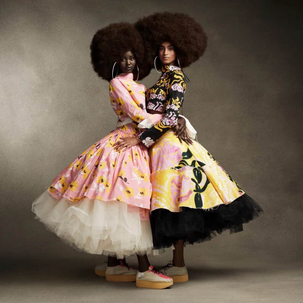 Two models in vibrant, patterned dresses with voluminous skirts and natural afro hairstyles.