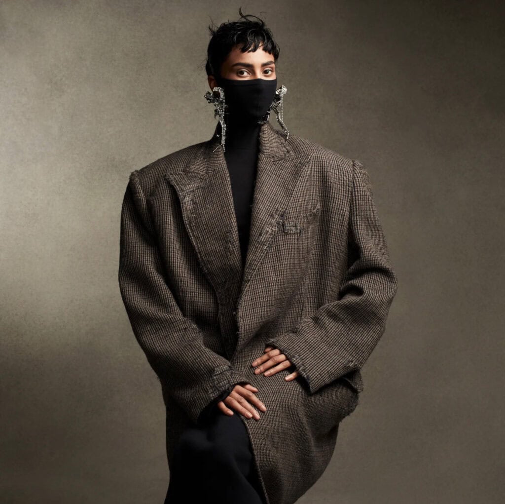 Model wearing oversized blazer with statement earrings and face mask.