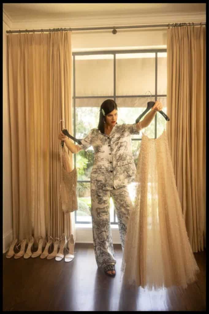 Alexandra Daddario in Dior dress fitting, holding fabric and accessories by the window.