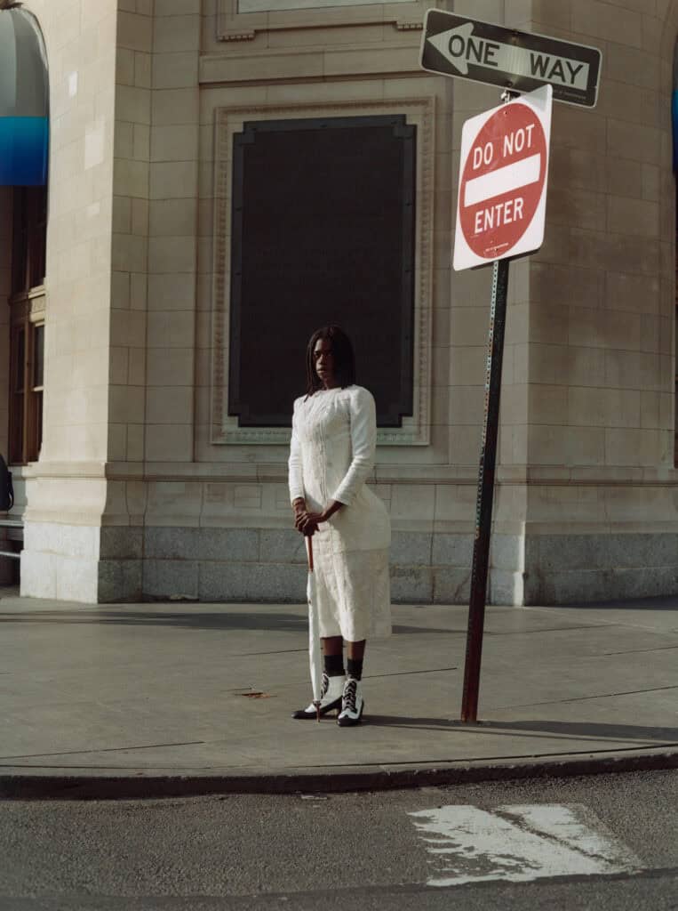 Elegant woman in white dress standing near street signs in urban setting.