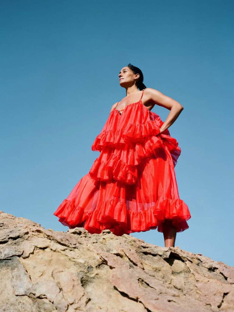 Elegant Tracee Ellis Ross in a vibrant red dress on rocky terrain.