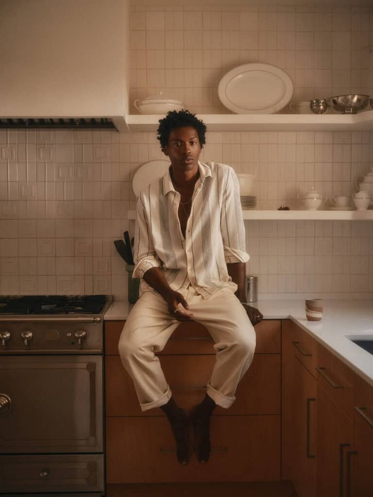 Stylish man in neutral outfit sitting on kitchen counter in Los Angeles, 2022.