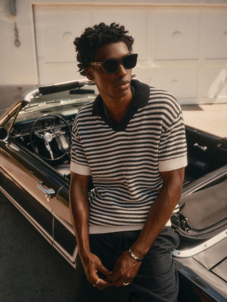 Stylish man wearing sunglasses and striped sweater in front of vintage car.