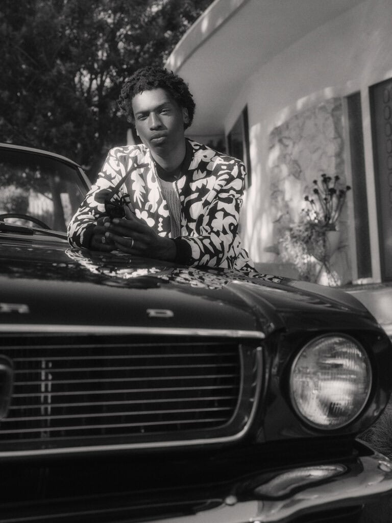 Stylish man with a patterned blazer leaning on a vintage car in Los Angeles.