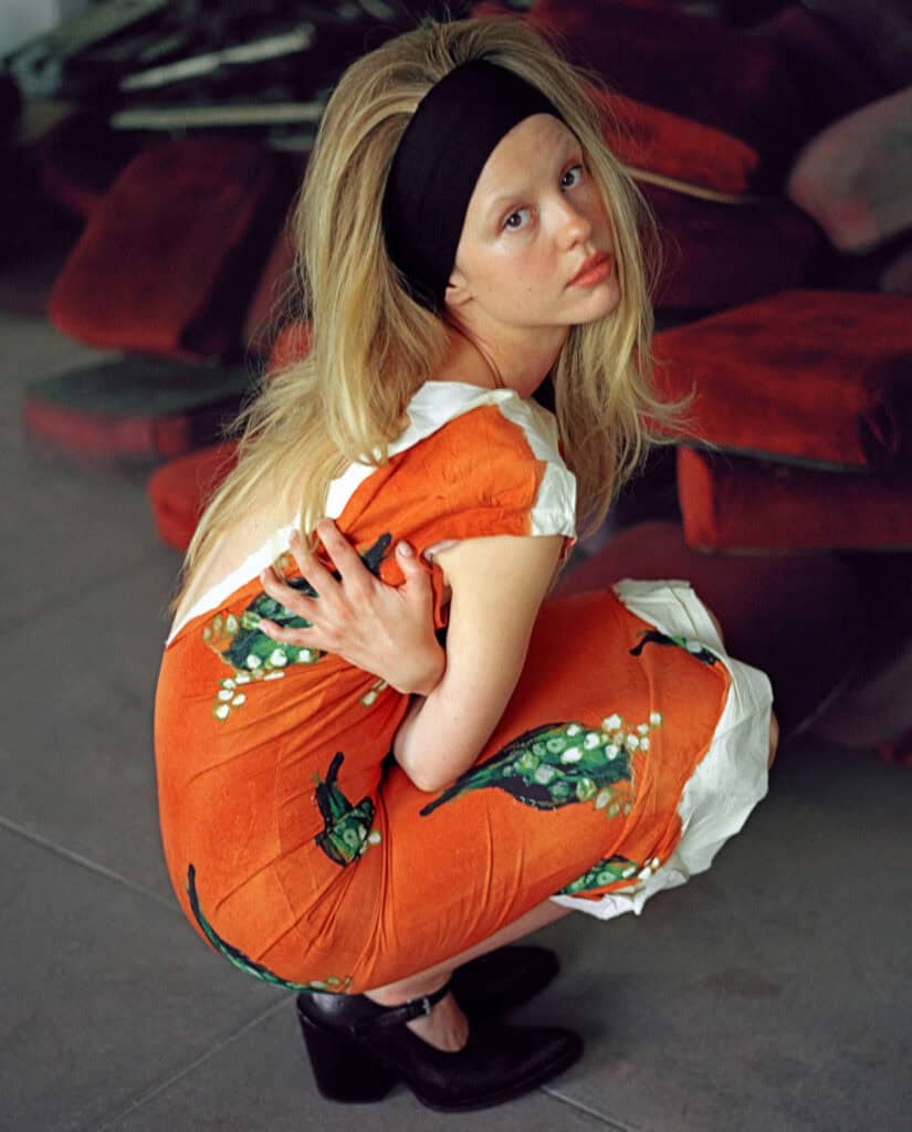 Young girl in floral orange dress with black headband, sitting on the floor at CULTURED MAGAZINE eve.