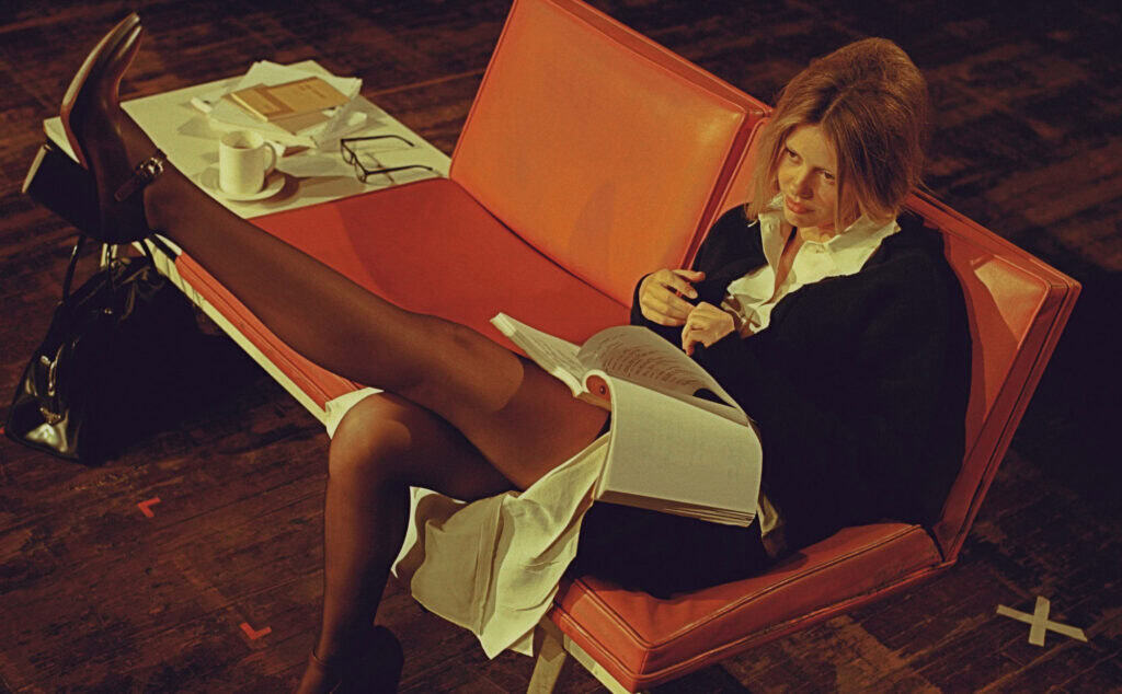 Woman reading on orange sofa with books and papers, CULTURED MAGAZINE.