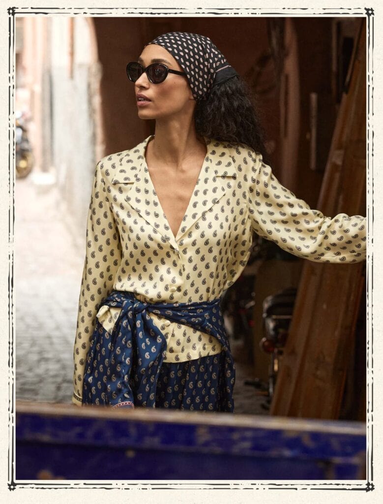 Woman in Moroccan street wearing Doen outfit, sunglasses, and headscarf.