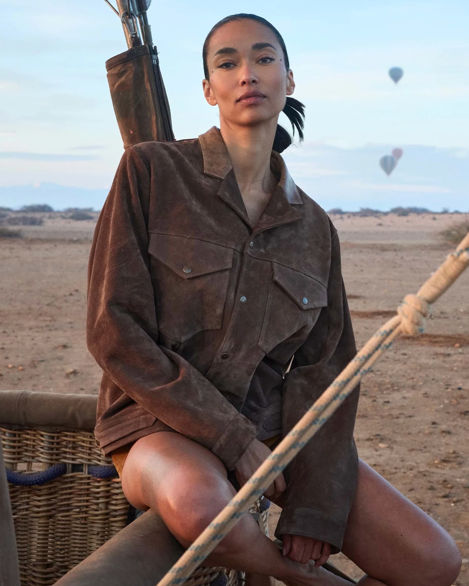 Woman in desert with hot air balloons in the background, Morocco.